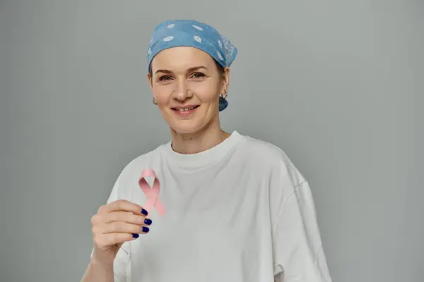 stock image A woman with short hair, wearing a casual outfit, smiles while holding a pink ribbon.