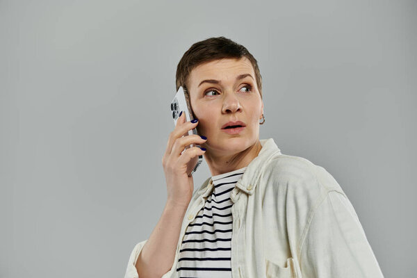 A woman with short hair holds a phone to her ear, looking surprised.