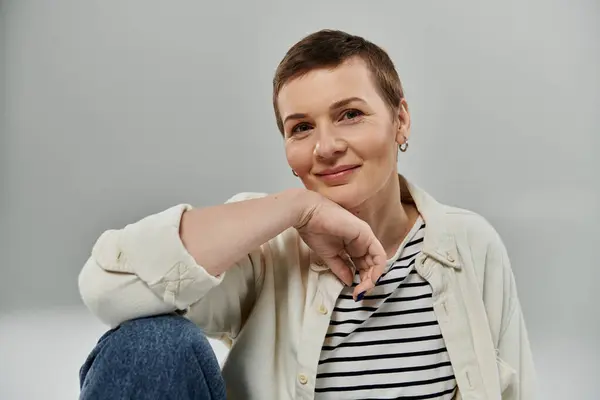 stock image A woman with short hair, wearing a white shirt and blue jeans, smiles and rests her chin on her hand.