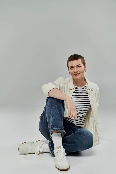 stock image A woman with short hair sits casually on a grey background, smiling confidently.