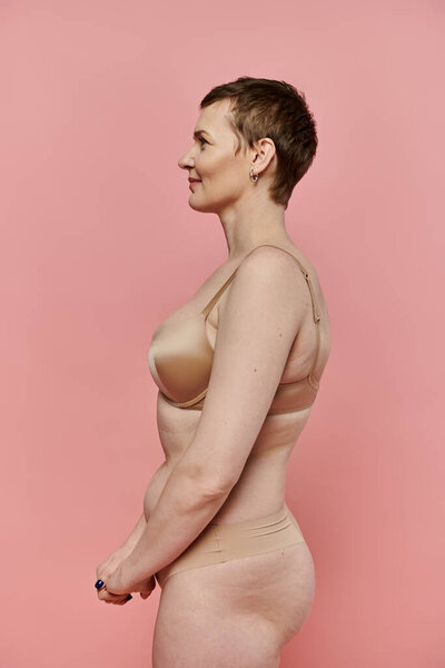 A woman with short hair stands in profile, wearing a bra