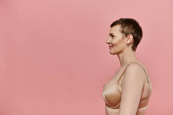 Короткошерстная женщина уверенно стоит на розовом фоне, символизируя осознание и профилактику рака молочной железы