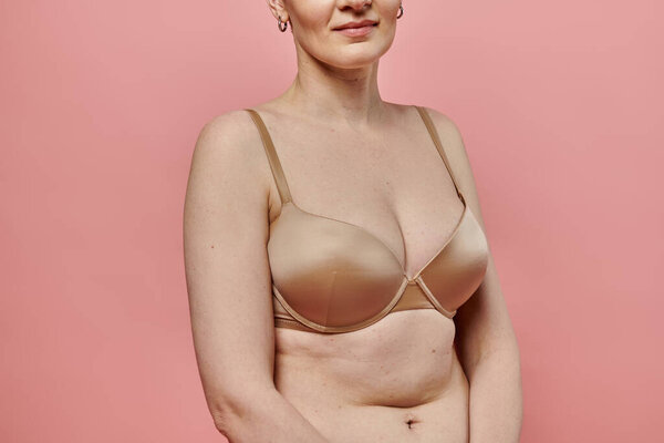 A woman stands against a pink backdrop, wearing a bra, promoting breast cancer awareness and prevention.