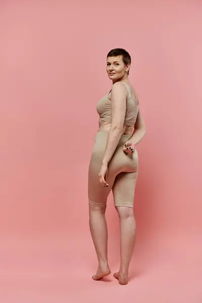 stock image A woman with short hair, wearing a bra, stands confidently against a pink background.