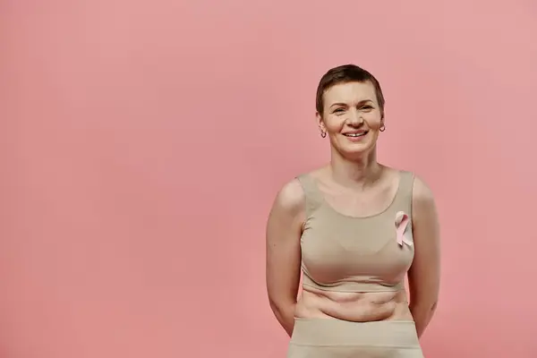 stock image A woman with short hair smiles confidently, wearing a pink ribbon in support of breast cancer awareness.