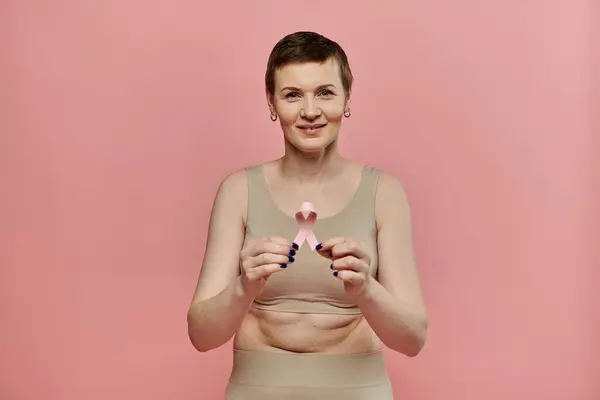 stock image A woman with short hair, wearing a bra and holding a pink ribbon, smiles at the camera.