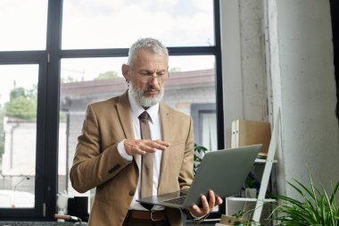 Olgun, sakallı bir LGBTQ öğretmeni arka planda penceresi olan modern bir ofiste online bir ders veriyor..