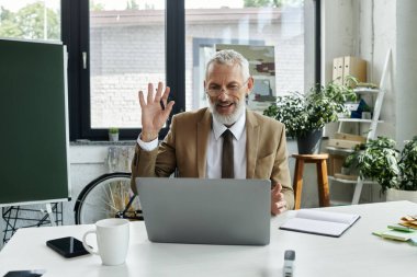 A mature teacher with a beard waves to his students during an online class, lgbtq member clipart