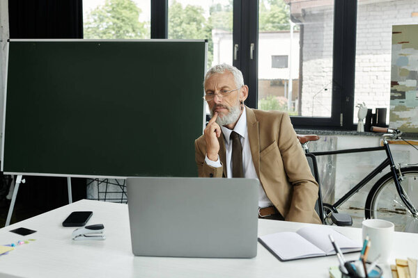 A bearded man sits at a desk with a laptop, preparing for an online class, lgbtq teacher