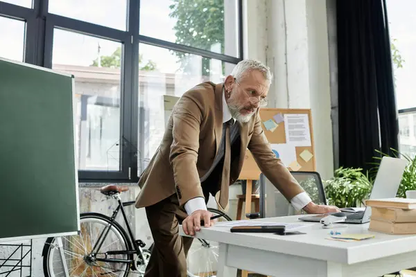 stock image A mature, bearded, lgbt teacher leans over his laptop, teaching a class online.