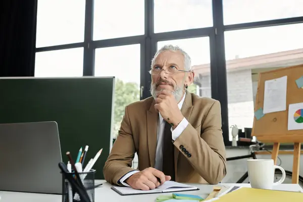 stock image A middle-aged man with a beard, wearing a suit, sits at a desk thoughtfully looking up while teaching online.