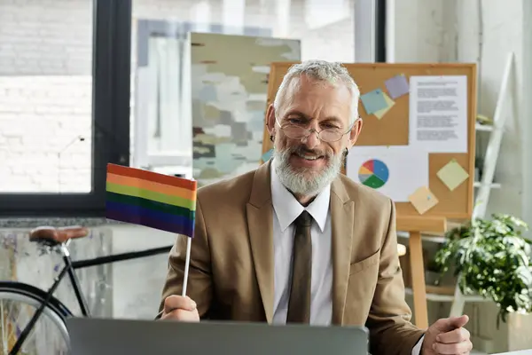 stock image A mature teacher with a beard smiles and holds a rainbow pride flag while teaching online.