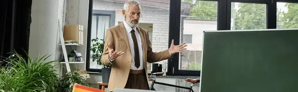 stock image A middle-aged teacher with a beard teaches a class online using a laptop and a whiteboard.