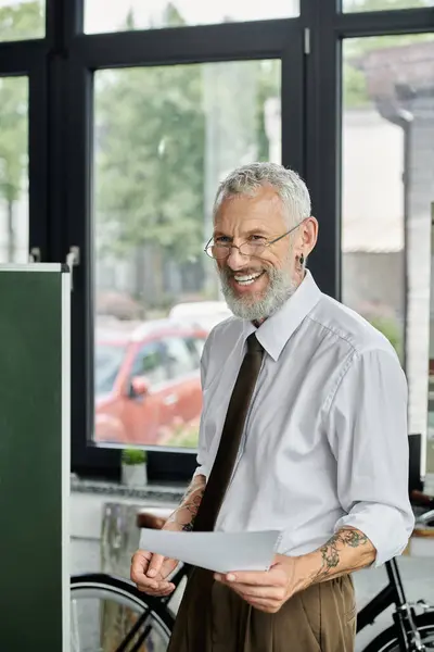 Stock image A bearded, middle-aged man smiles as he holds a paper in front of a green board.