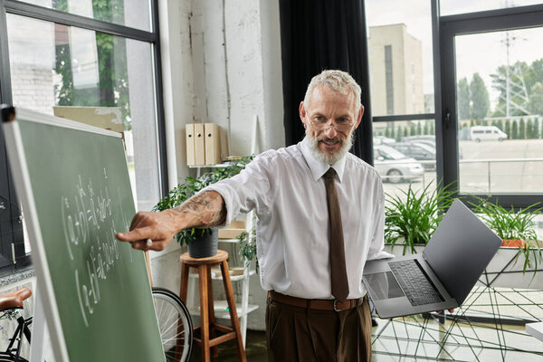 A mature LGBTQ teacher with a beard teaches math online, using a laptop and a blackboard.