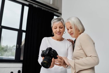 Olgun bir lezbiyen çift fotoğraf stüdyosunda birlikte fotoğraf çektirirken, bir kadın kamerayı tutarken diğeri ekrana bakıyor..