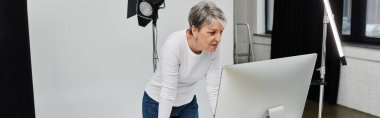 A woman in a white shirt bends over a computer screen, likely reviewing photos of a photoshoot. clipart