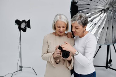 Olgun bir lezbiyen çift fotoğraf stüdyosunda poz veriyor, biri kamerayı tutarken diğeri çekim için modellik yapıyor..
