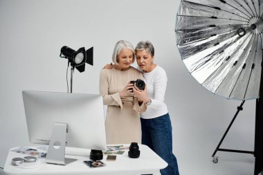 İki kadın, bir fotoğrafçı ve onun modeli, bir stüdyo ortamında iş birliği yapıyorlar, bir kameradaki görüntüleri inceliyorlar..