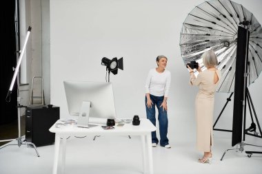Lezbiyen bir çift stüdyoda fotoğraf çekimi için poz veriyor. Uzun elbiseli fotoğrafçı, ortağının resmini çeker..
