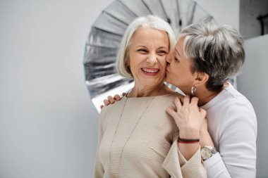 Olgun bir lezbiyen çift fotoğraf stüdyosunda bir portre için poz verir. Birbirlerini yanaklarından öperlerken sevgi dolu olurlar..