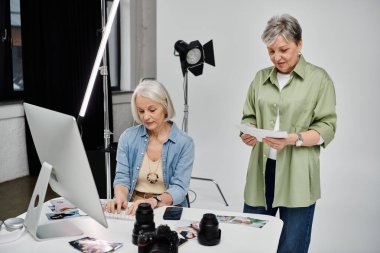 Lezbiyen bir çift fotoğraf stüdyosunda. Bir kadın bilgisayardaki fotoğrafları incelerken diğer kadın da incelemek için fotoğrafları tutuyor..
