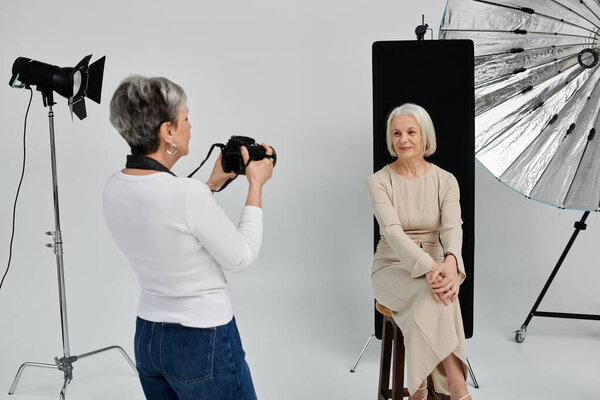 Woman photographs partner in studio. Photographer focuses on subject, while model confidently looks at the camera from a stool