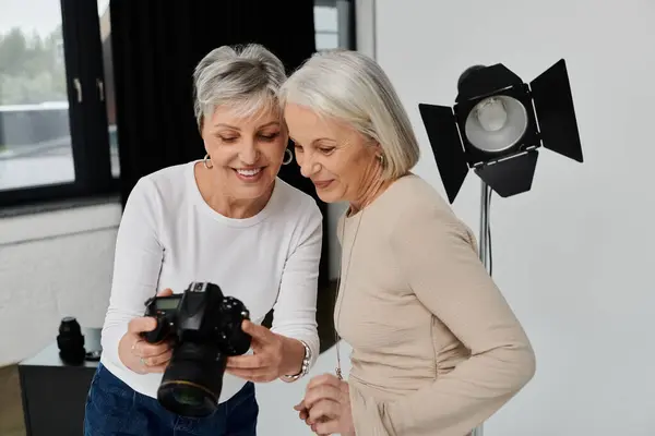 stock image A mature lesbian couple in a photo studio, one holding a camera while the other poses as the model.