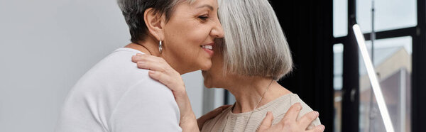 Two mature women embrace during a photo shoot.