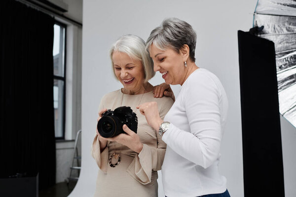 A photographer and her model, a loving lesbian couple, laugh together while reviewing a photo in a studio setting.