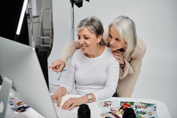 Две зрелые женщины вместе смотрят на экран компьютера в фотостудии.