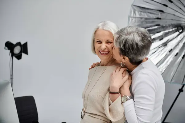 stock image Two mature women, dressed in casual clothes, share a loving kiss during a photoshoot in a studio setting.