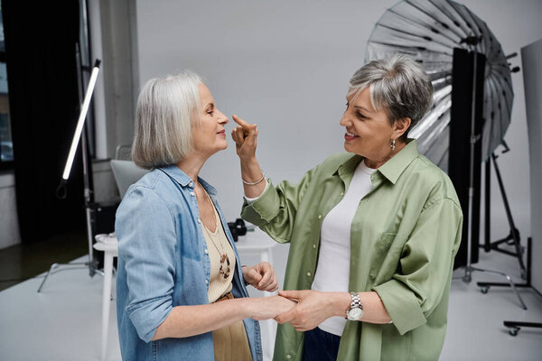 A photographer gently touches the model's nose as they laugh together in a studio setting.
