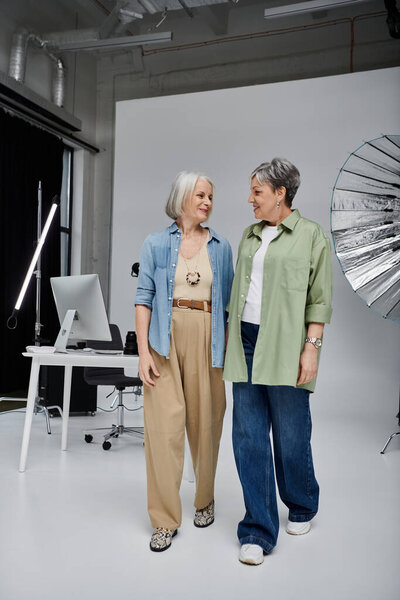 Two women, dressed casually, stand in a photo studio.