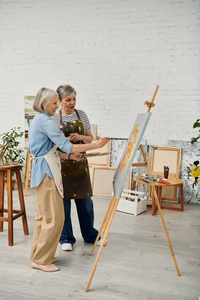 stock image Two mature lesbian women, one painting on a canvas, the other giving instructions.