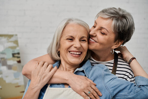 Two women, embracing in an art studio, laugh together as they paint and share their creative passion.