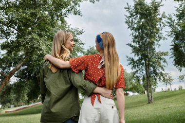 Lezbiyen bir çift yeşil bir parkta el ele yürür, güneşli bir günün tadını çıkarırlar..