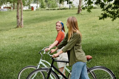 Genç lezbiyen bir çift, bisikletleriyle yemyeşil bir parkta romantik bir öğleden sonranın tadını çıkarıyor..