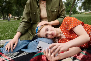 Genç bir lezbiyen çift yeşil bir parkta battaniyede dinlenirken hassas bir anı paylaşıyor..