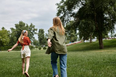 Sıradan giyinmiş iki genç kadın, yaz öğleden sonra yeşil bir parkta koşuyorlar..