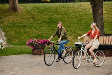 Two young women are on a bike ride in a park. clipart