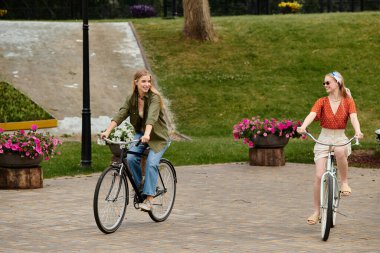 Two young women enjoy a sunny day riding bikes in a green park. clipart