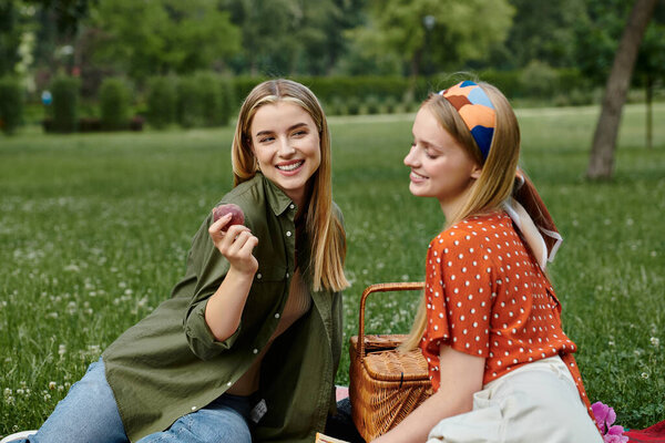 A lesbian couple enjoys a romantic picnic in a lush green park, sharing a snack and a laugh.