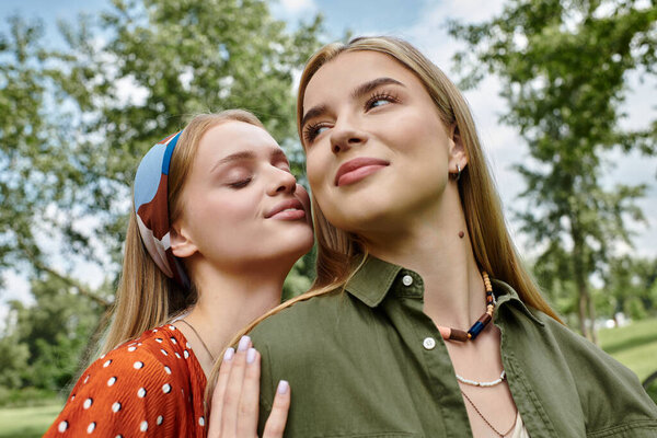 Two women embrace in a green park, their eyes locked in a loving gaze.