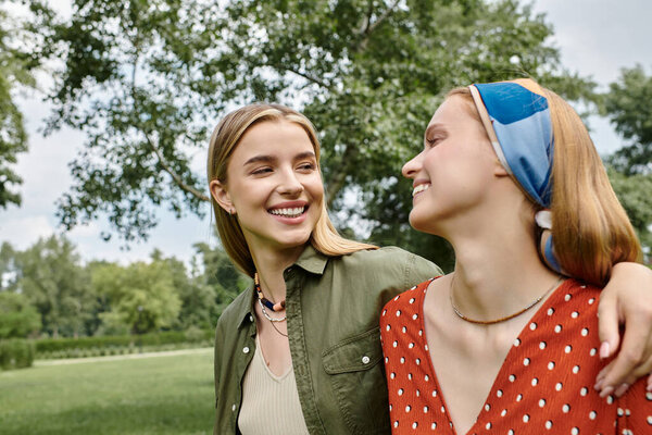 Two young women laugh and embrace during a sunny day in the park.