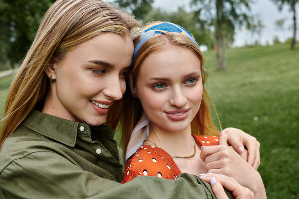 Two young women embrace in a lush green park, enjoying a romantic moment on a sunny day.