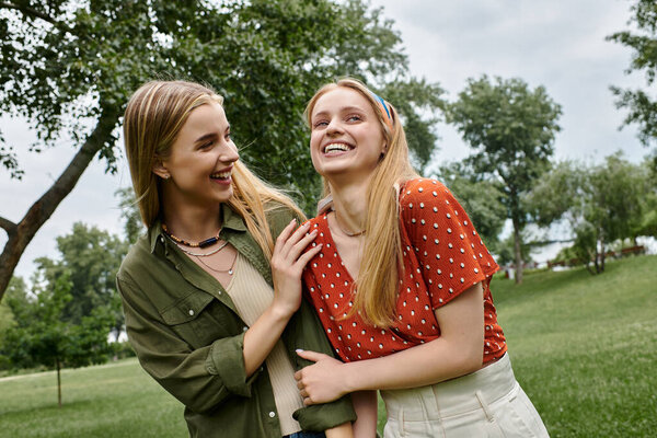 Two women laugh together on a sunny day in the park.