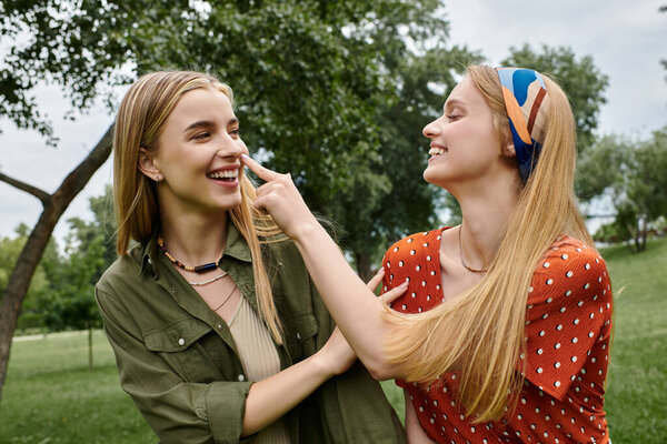 Two young women laugh together in a grassy park, enjoying each other company.