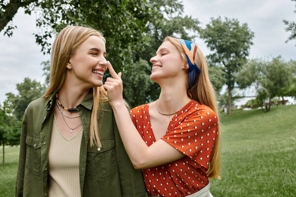 Two young women laugh together while enjoying a date in a green park.