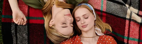 stock image A young lesbian couple lie together on a red and black checkered blanket in a green park, enjoying a peaceful moment.